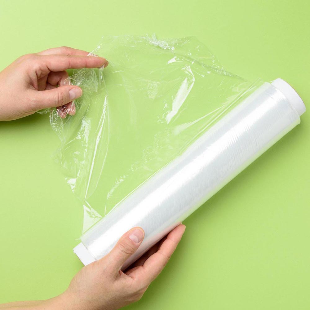 To kvinnelige hender holder en rull med gjennomsiktig klamfilm for emballasjeprodukter, grønn bakgrunn